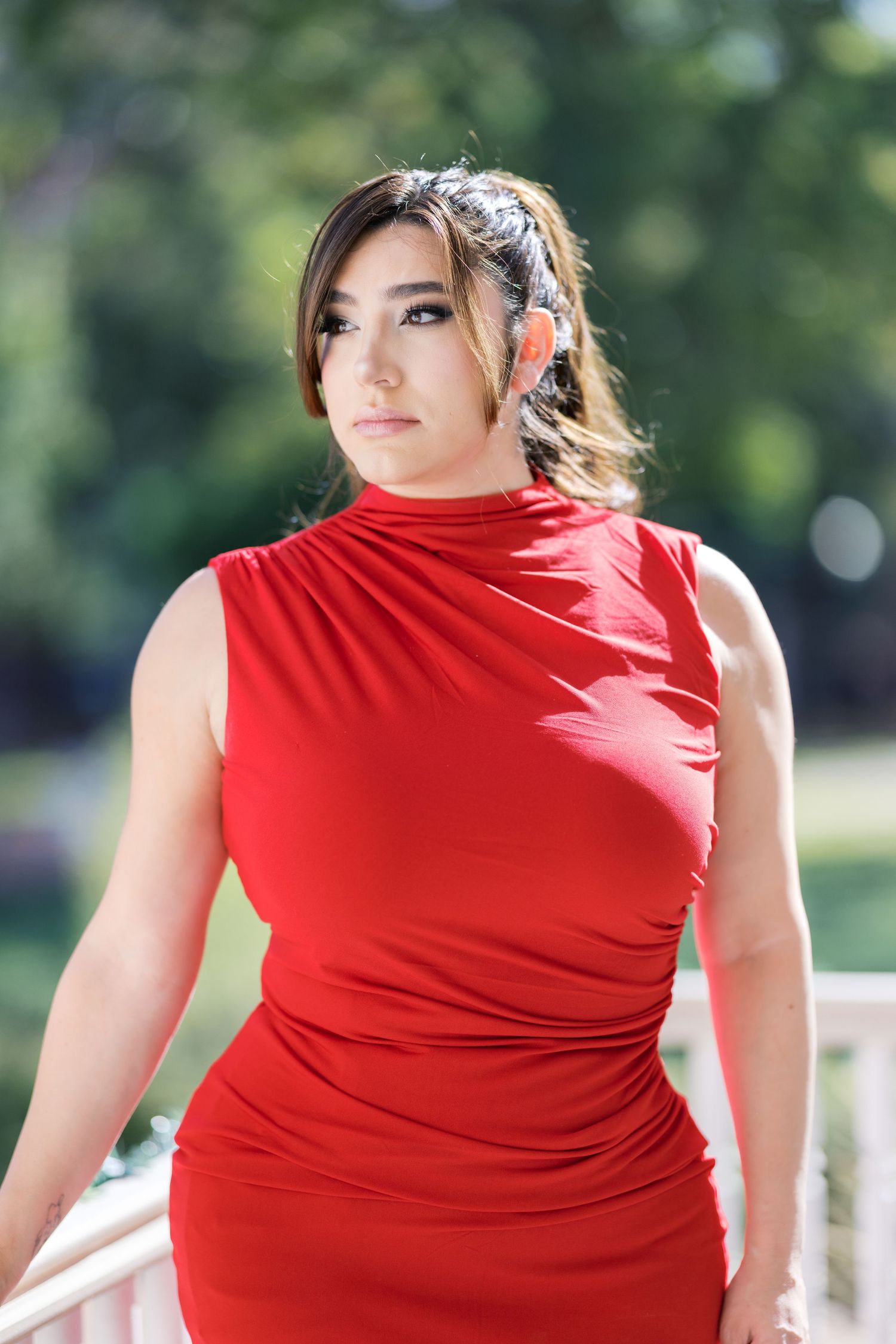 Side view of red sleeveless dress against green outdoor setting.