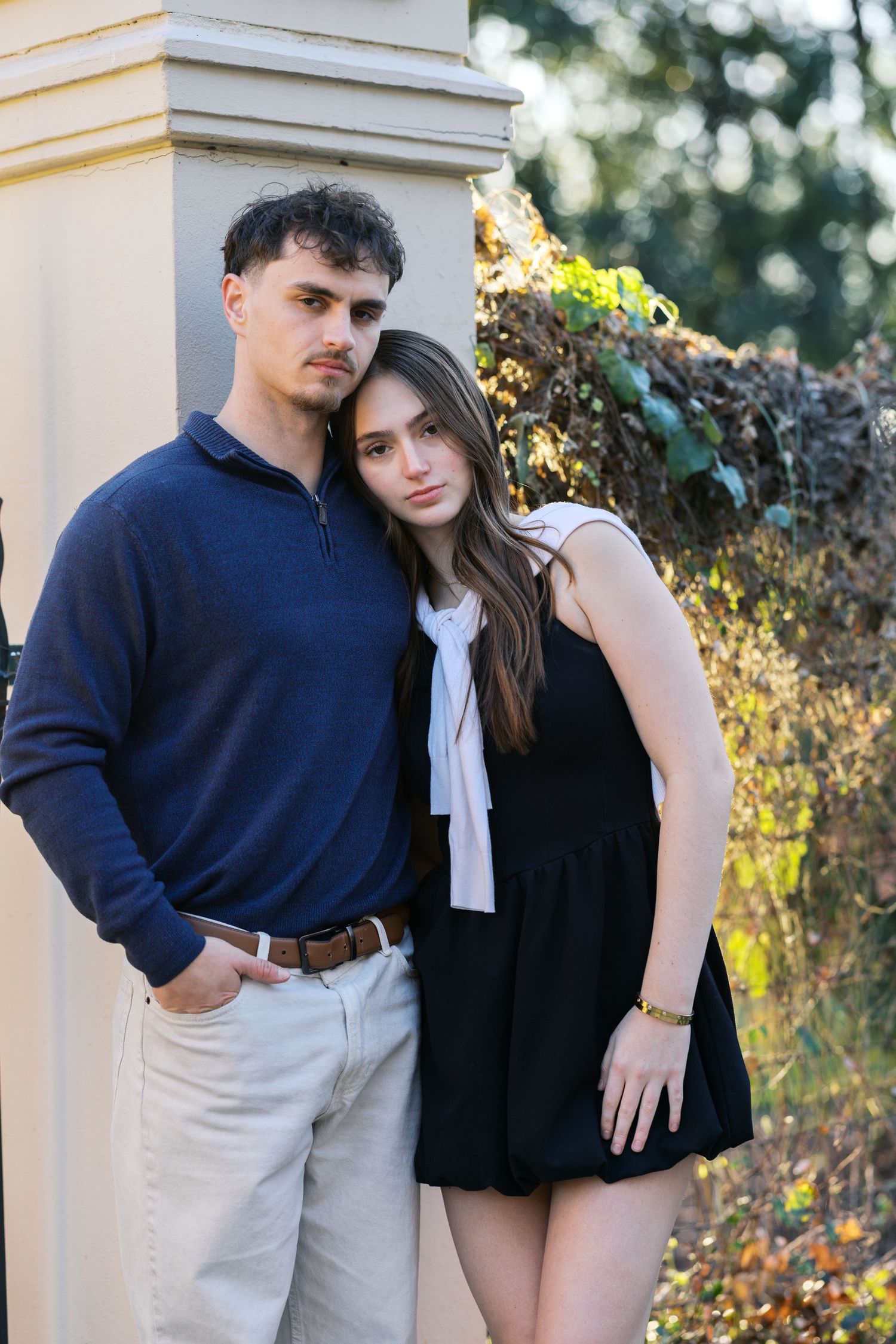 Young couple leaning against a pillar outdoors, woman resting her head on mans shoulder.