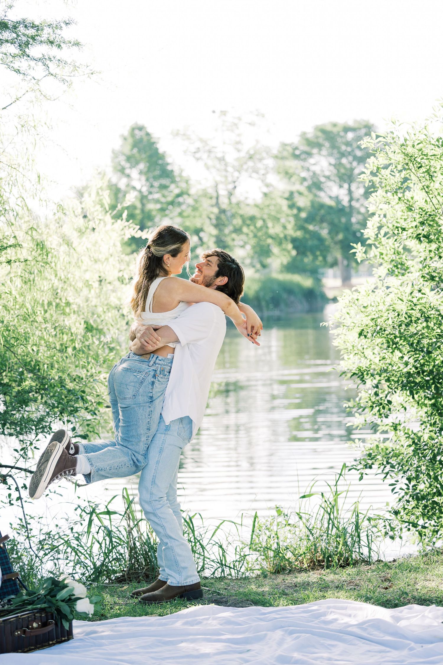 A couple sharing a joyful embrace near a serene lake on a sunny afternoon.
