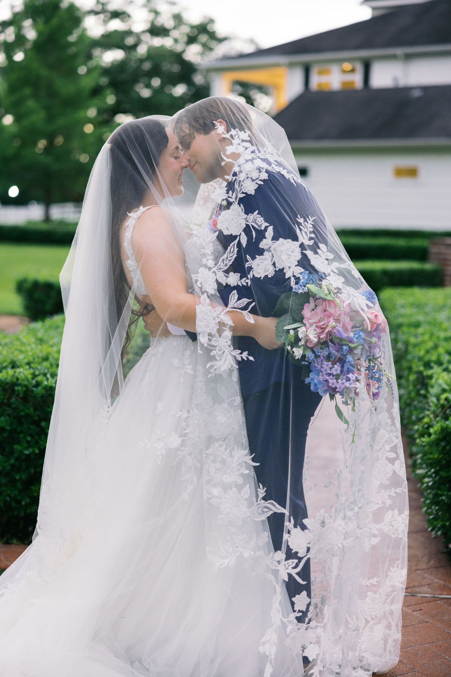 Romantic wedding photos showing the intricate details of a white lace veil against a navy suit.