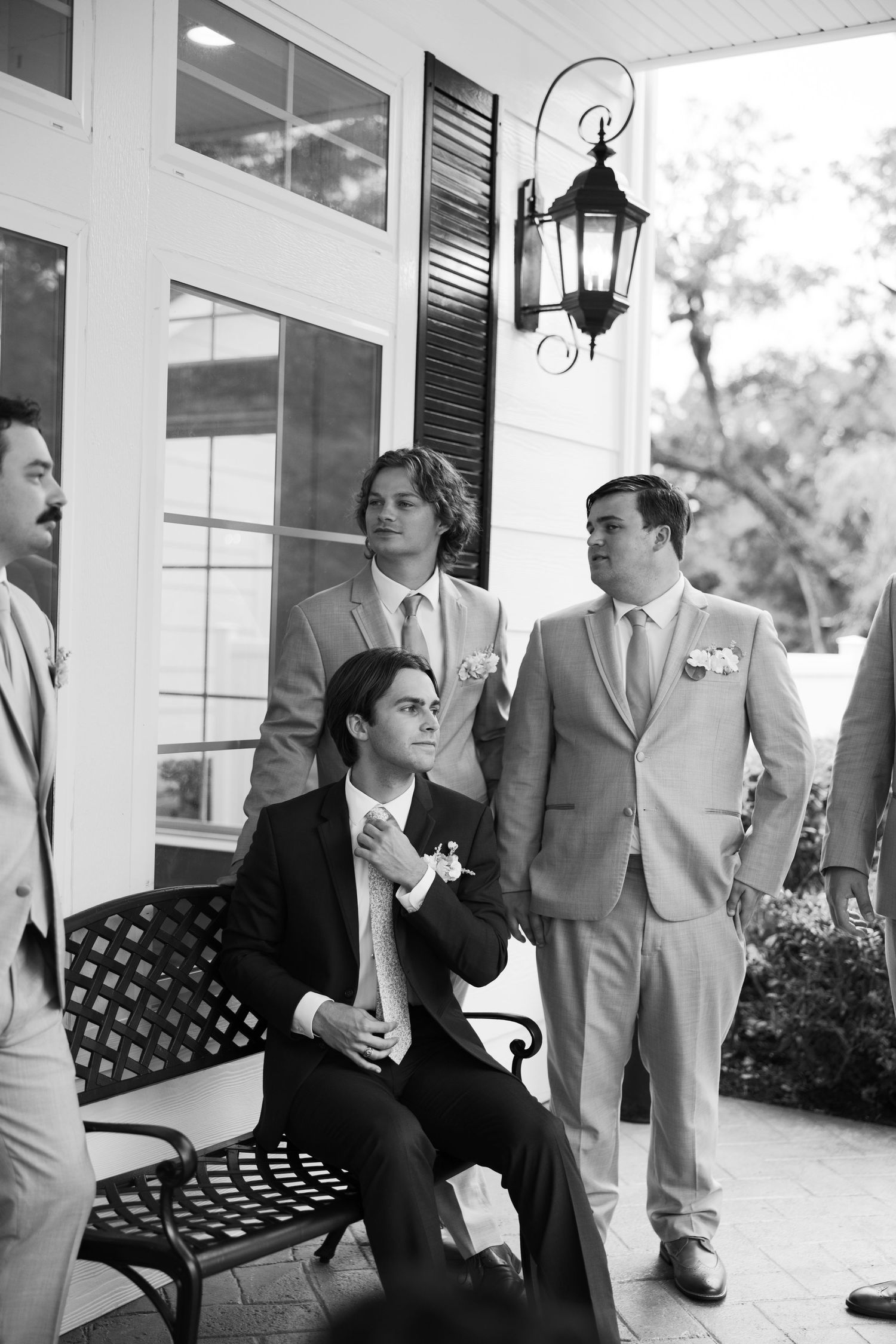 Wedding party relaxing on porch bench in formal attire at elegant venue.