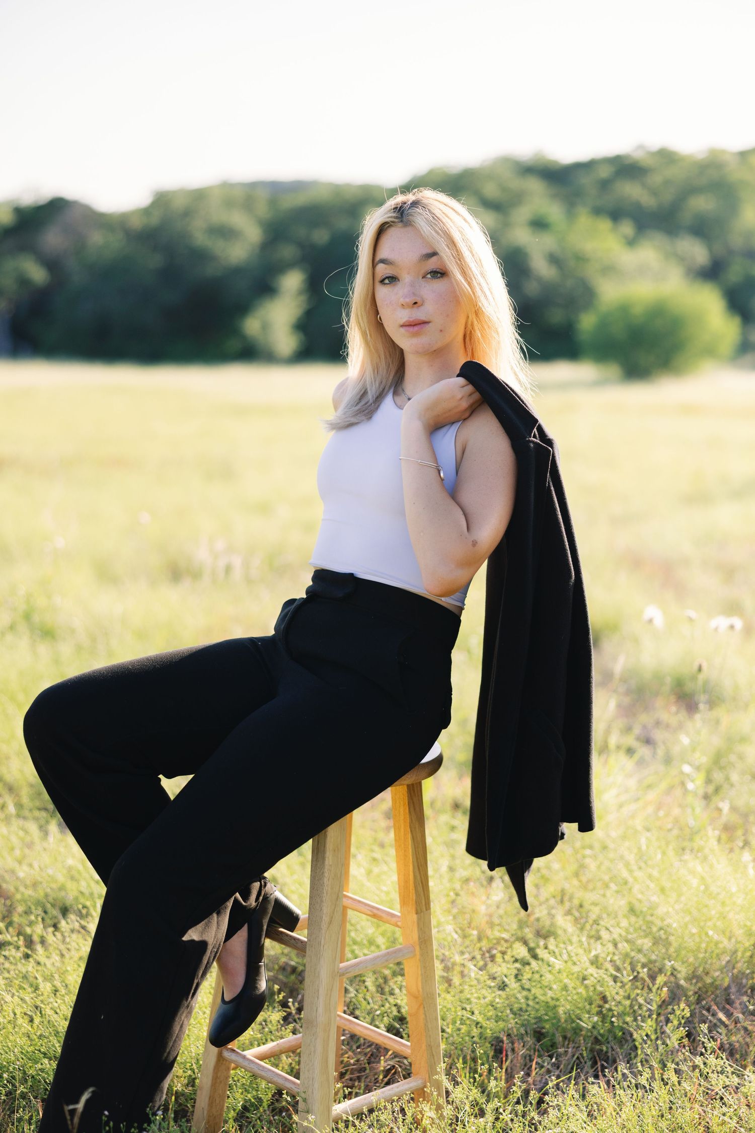 Fashion portraits on wooden stool in grassy field during sunset.