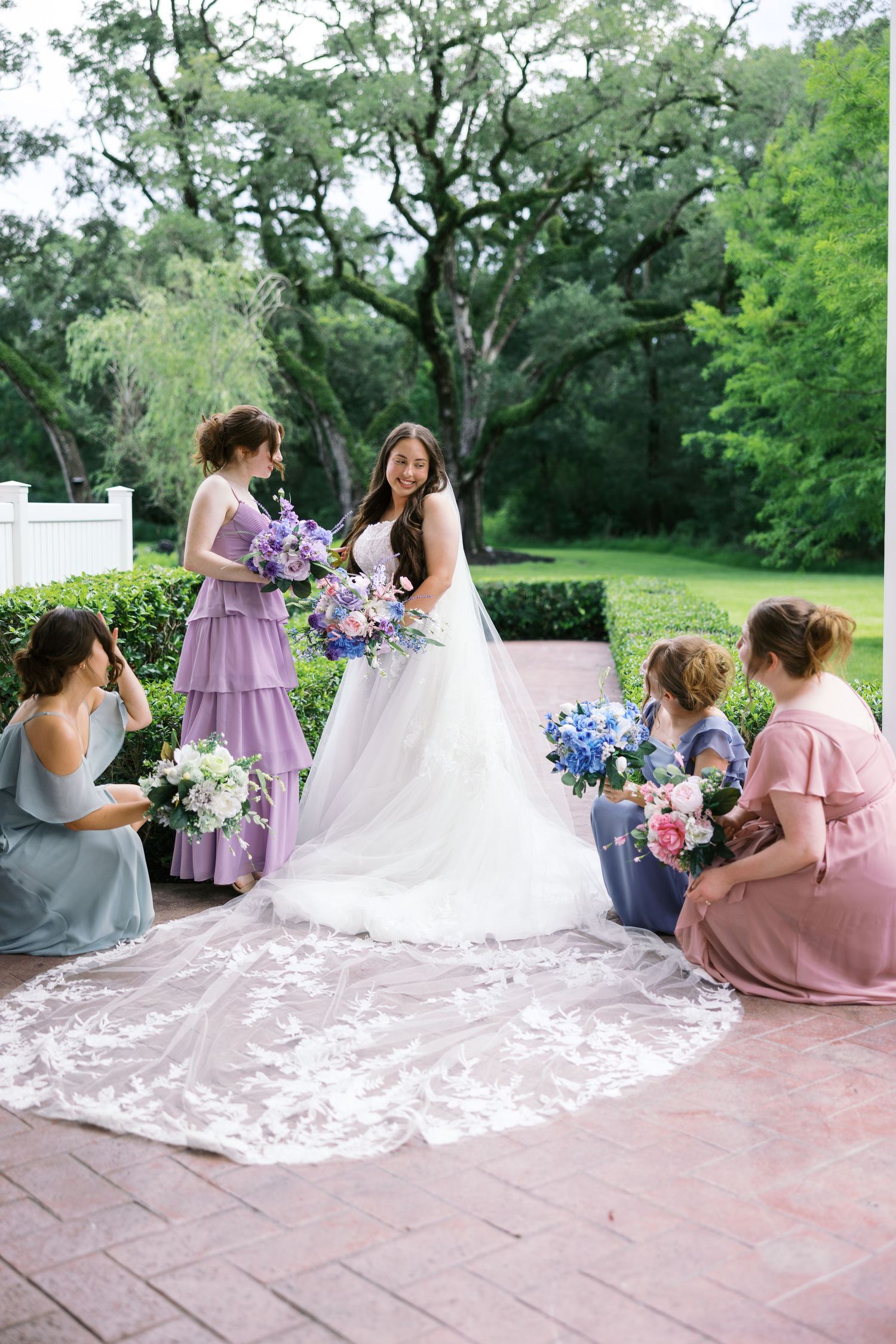 Wedding party in pastel dresses relaxing on patio with bride's long train spread out.
