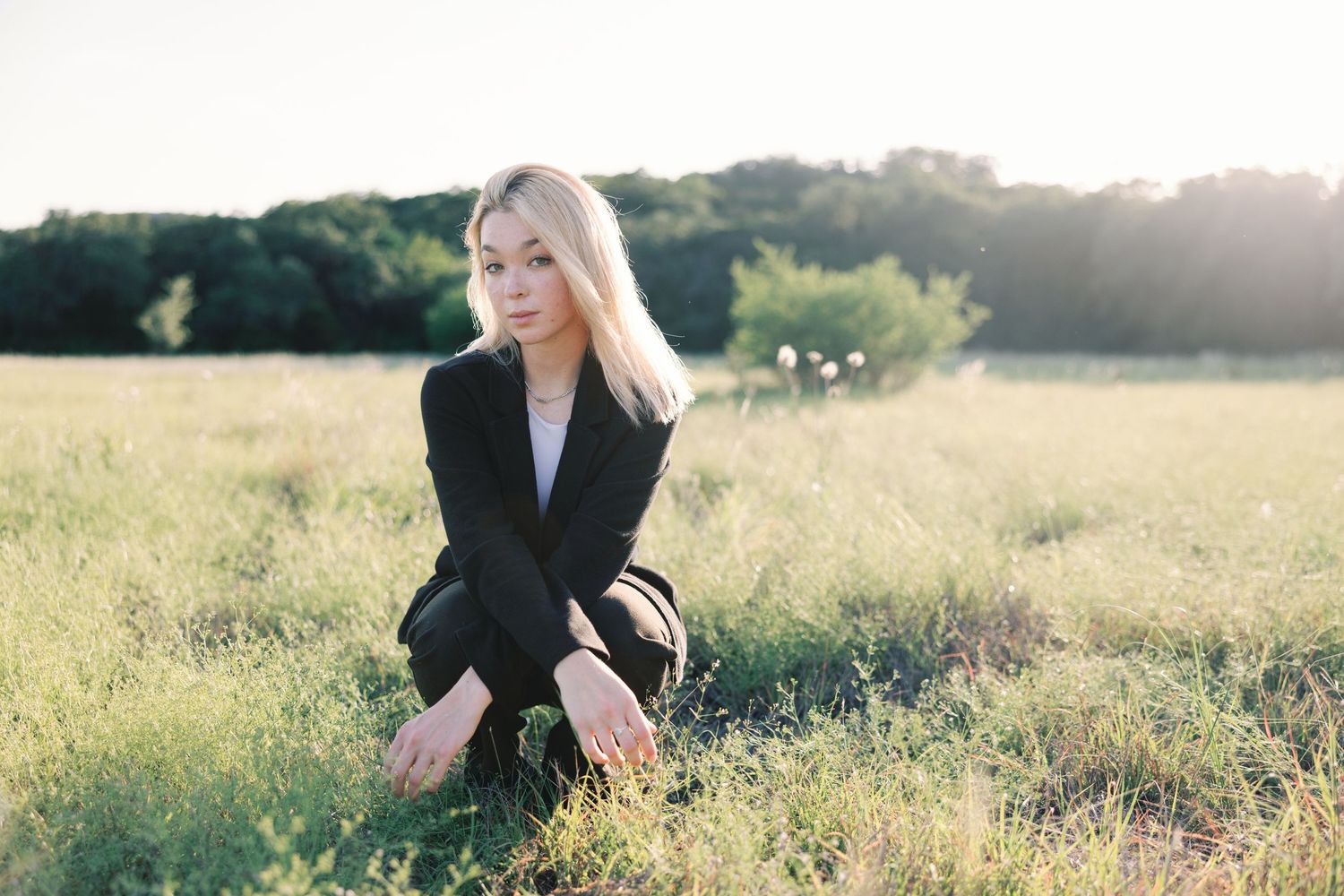 Artistic portrait series in a sunlit meadow with black blazer against golden hour lighting.