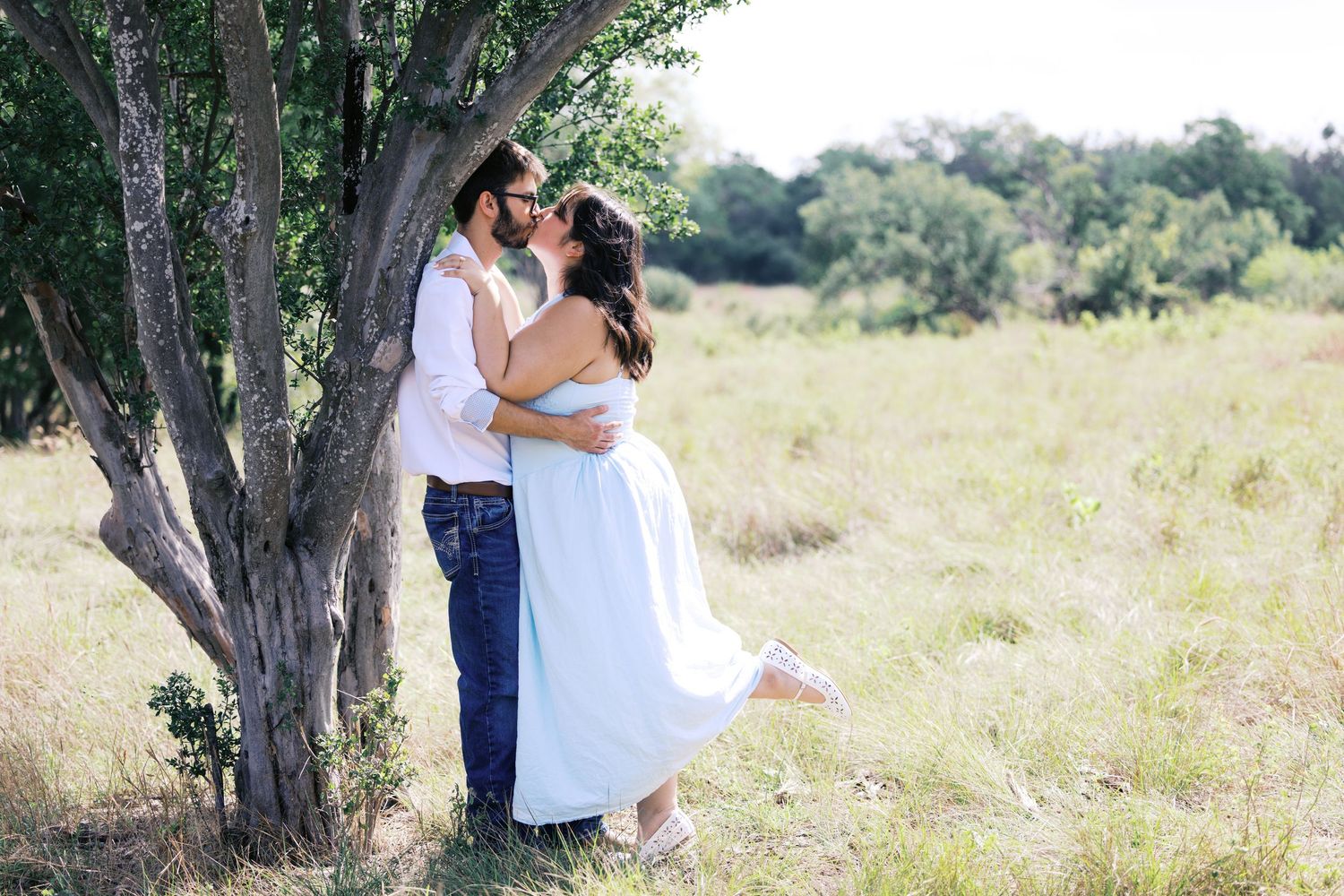 A couple shares an intimate moment under trees in a natural outdoor setting.