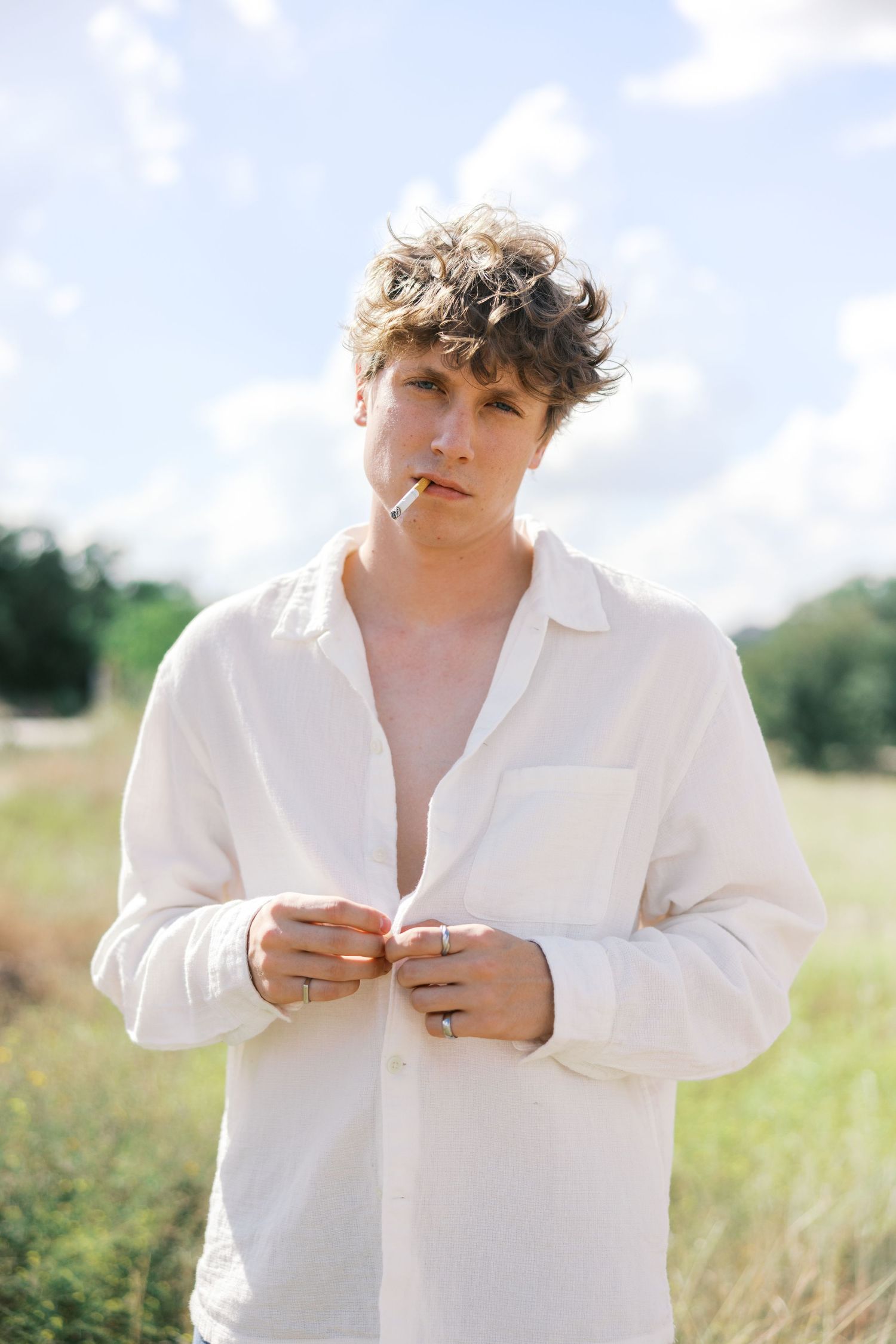 Candid moment captured in sunlit field wearing casual white button-down shirt.