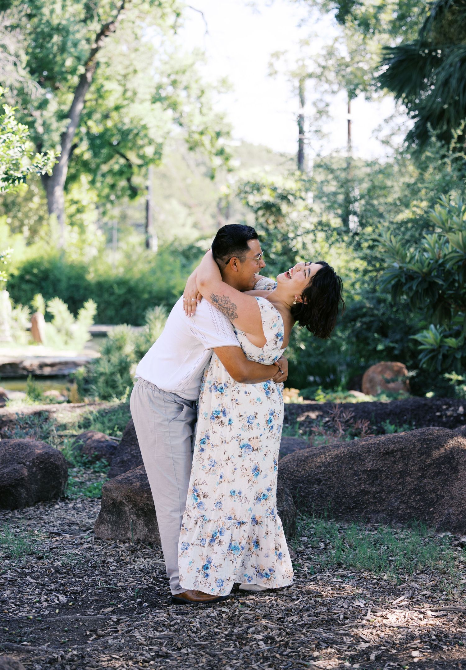 A couple shares a romantic dance moment in a garden setting with rocks and trees.