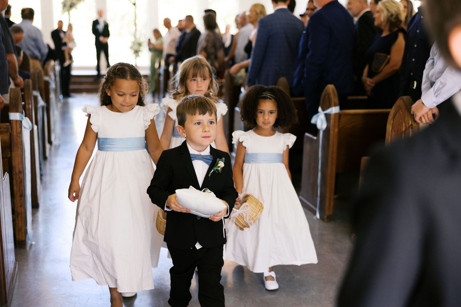 Ring bearer and flower girls walking down church aisle during wedding ceremony.