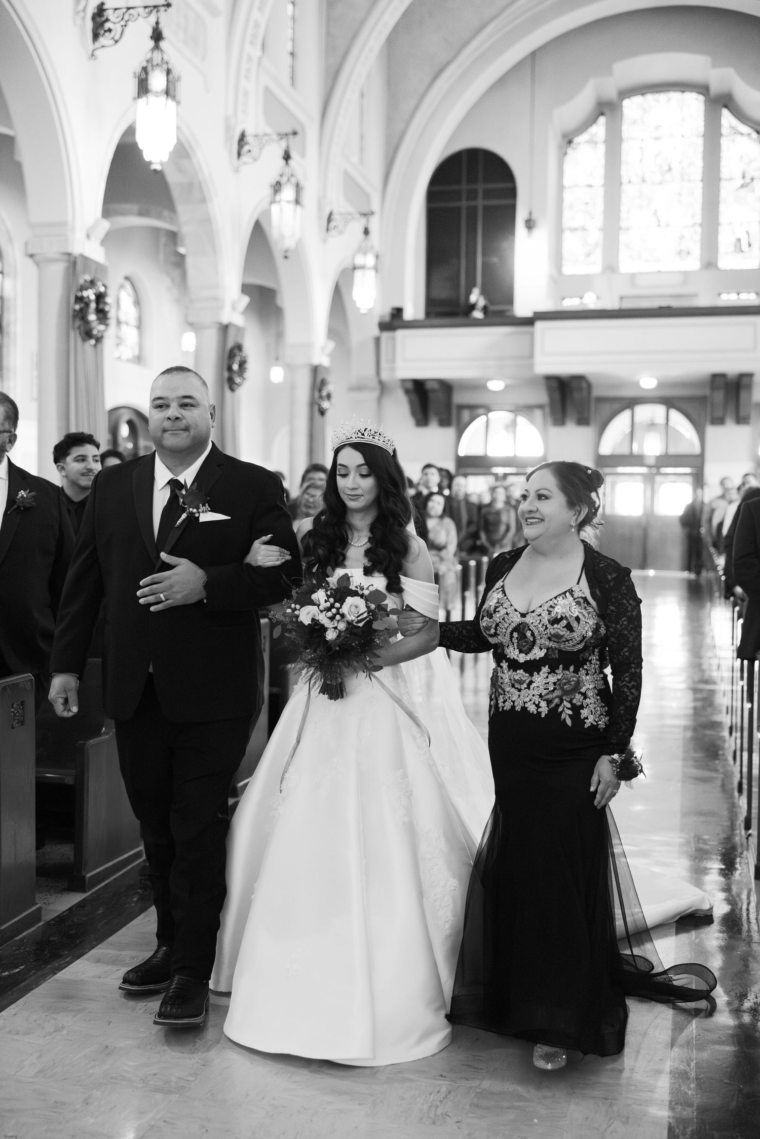Wedding party members walking down the aisle in a grand church with arched ceilings and ornate architecture.