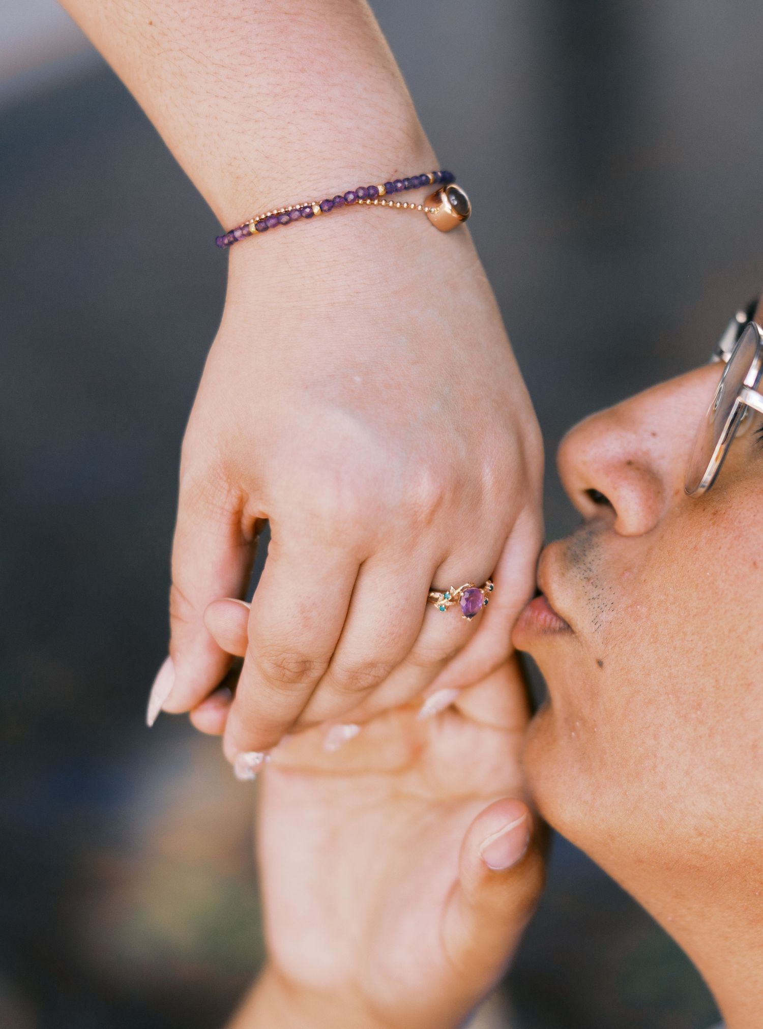 A close-up of hands with a delicate beaded bracelet and ring being kissed.