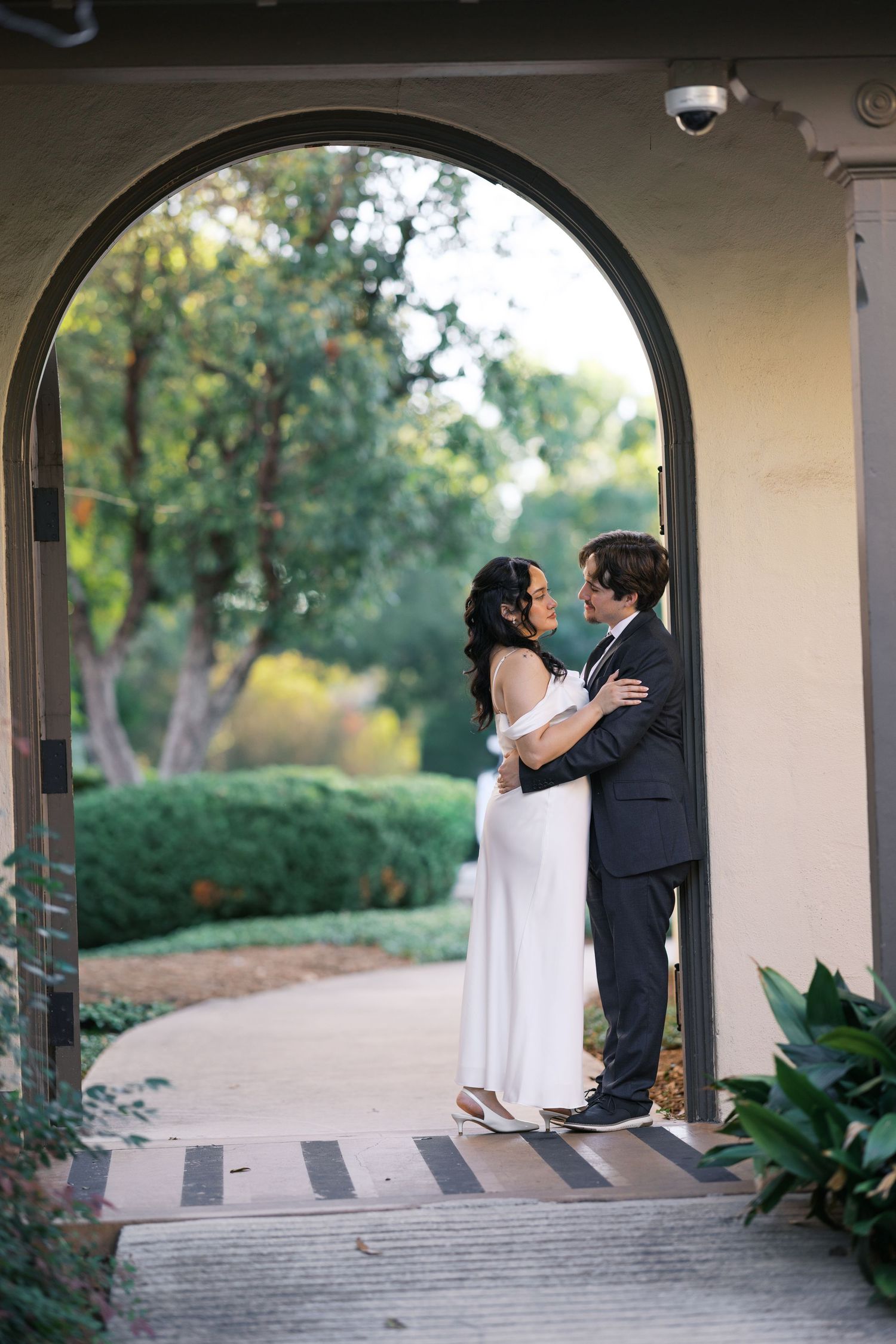 Romantic couple sharing intimate moments under arched walkway with greenery in background.