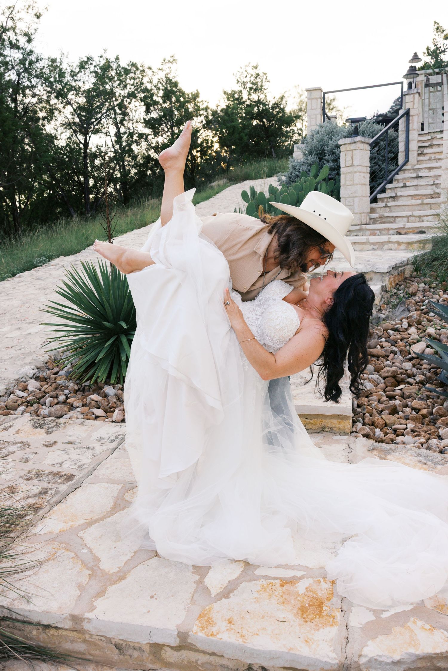 Bride in flowing white dress twirling dramatically on stone patio with desert backdrop.