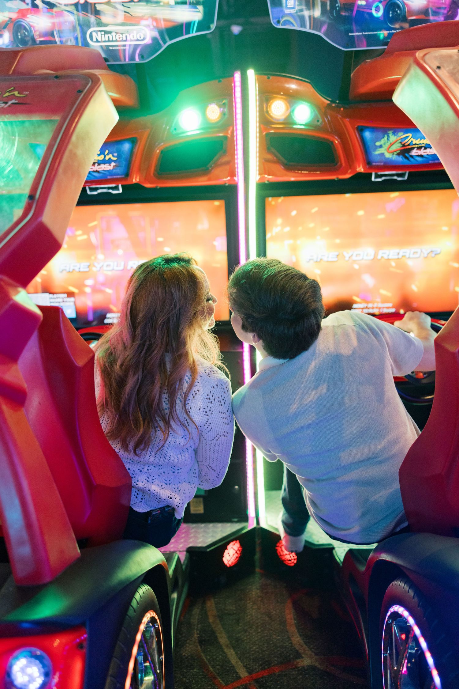 Two people playing arcade games with colorful neon lights in the background.