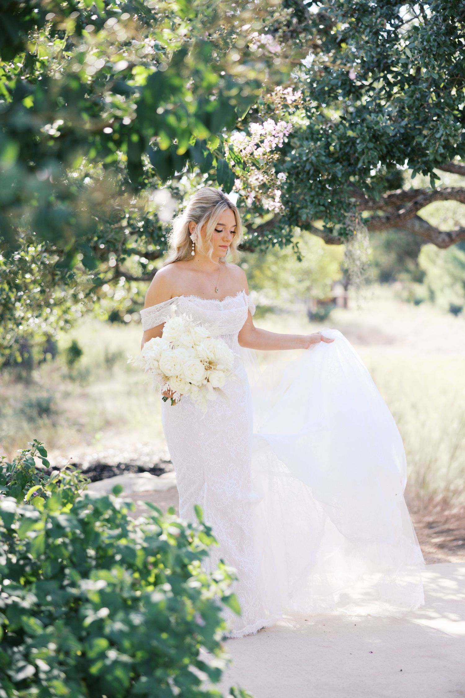 Ethereal bridal portrait with flowing white gown against sunlit garden backdrop.
