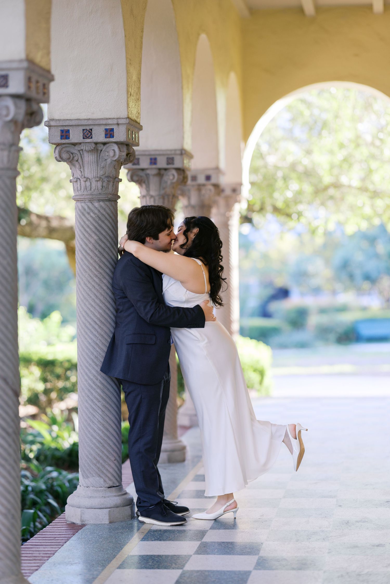 A romantic wedding photoshoot in a columned walkway with natural lighting and elegant architecture.