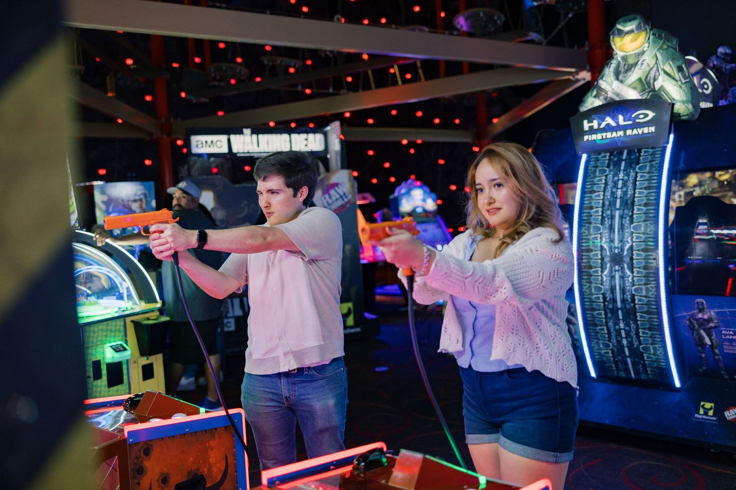 People playing shooting games in a dark arcade with neon lighting.