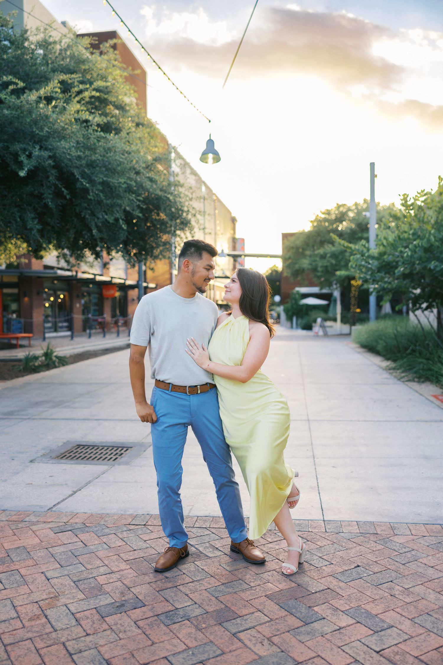 Couple walking and posing playfully on brick-paved outdoor walkway.