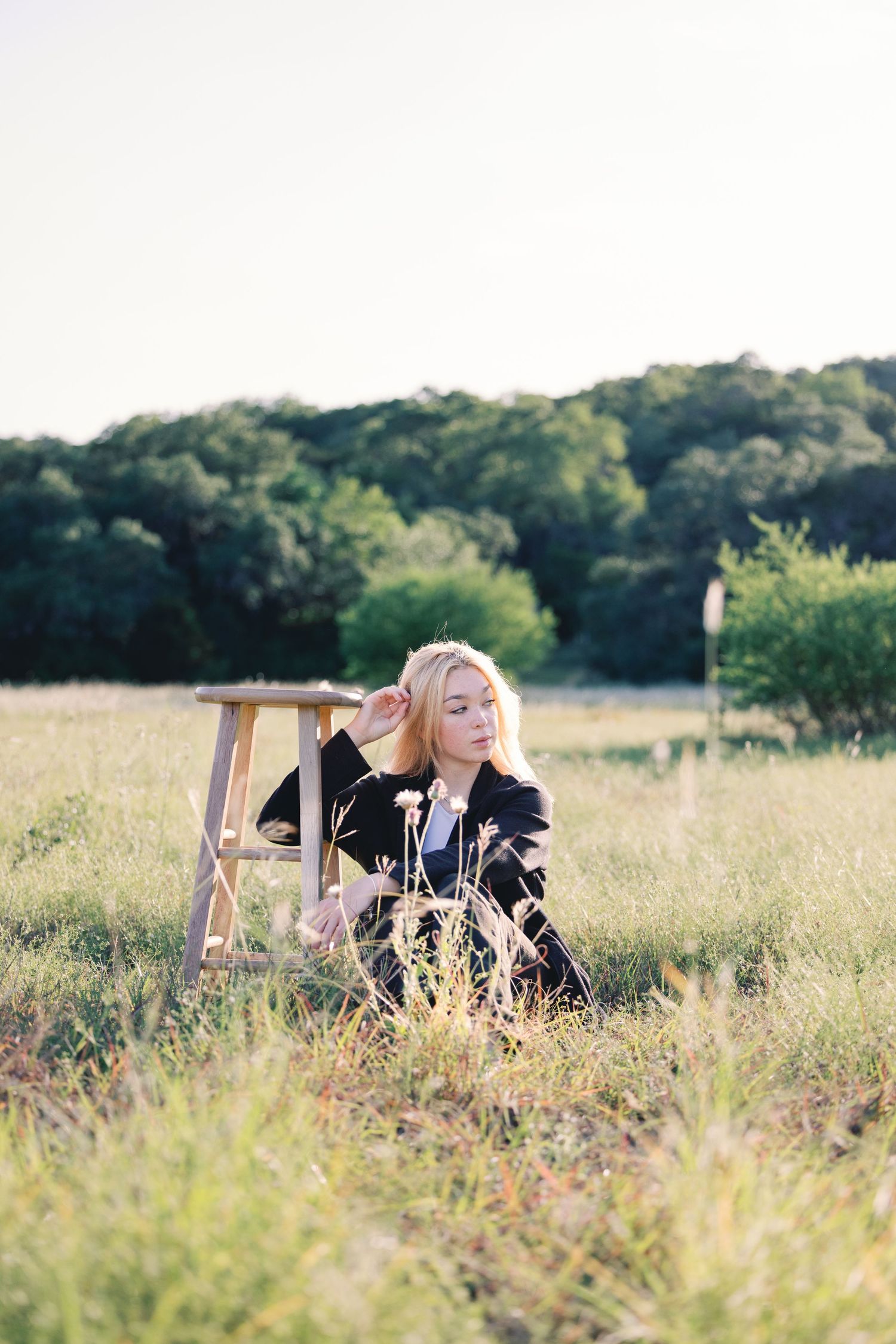 Figure relaxing on wooden stool amidst wild grasses in golden afternoon light.