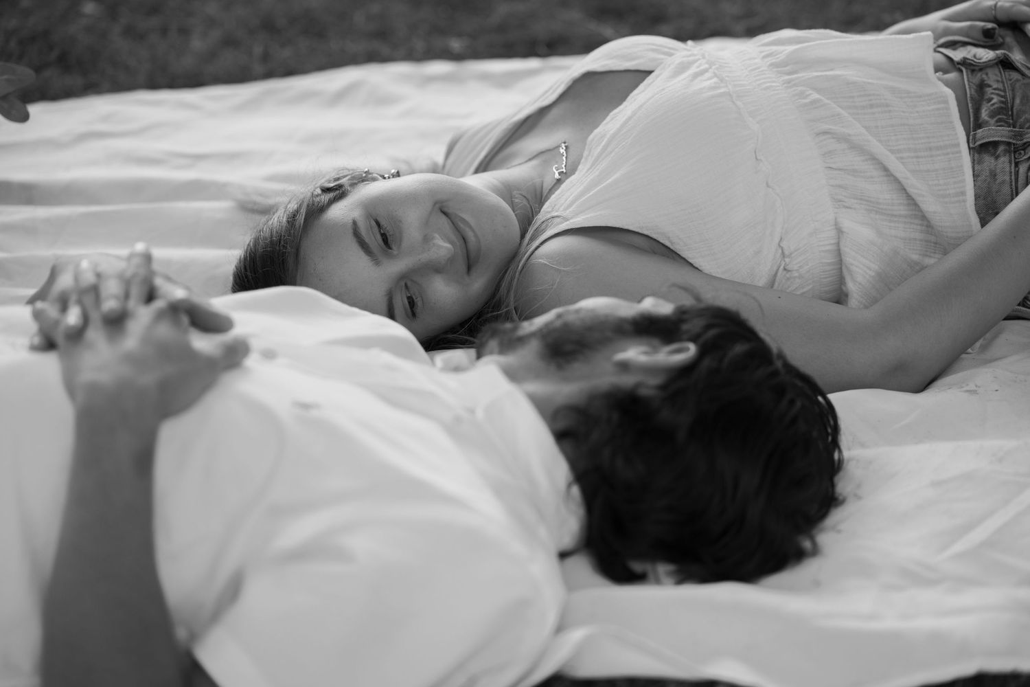 A couple lies peacefully on a white blanket in black and white tones.