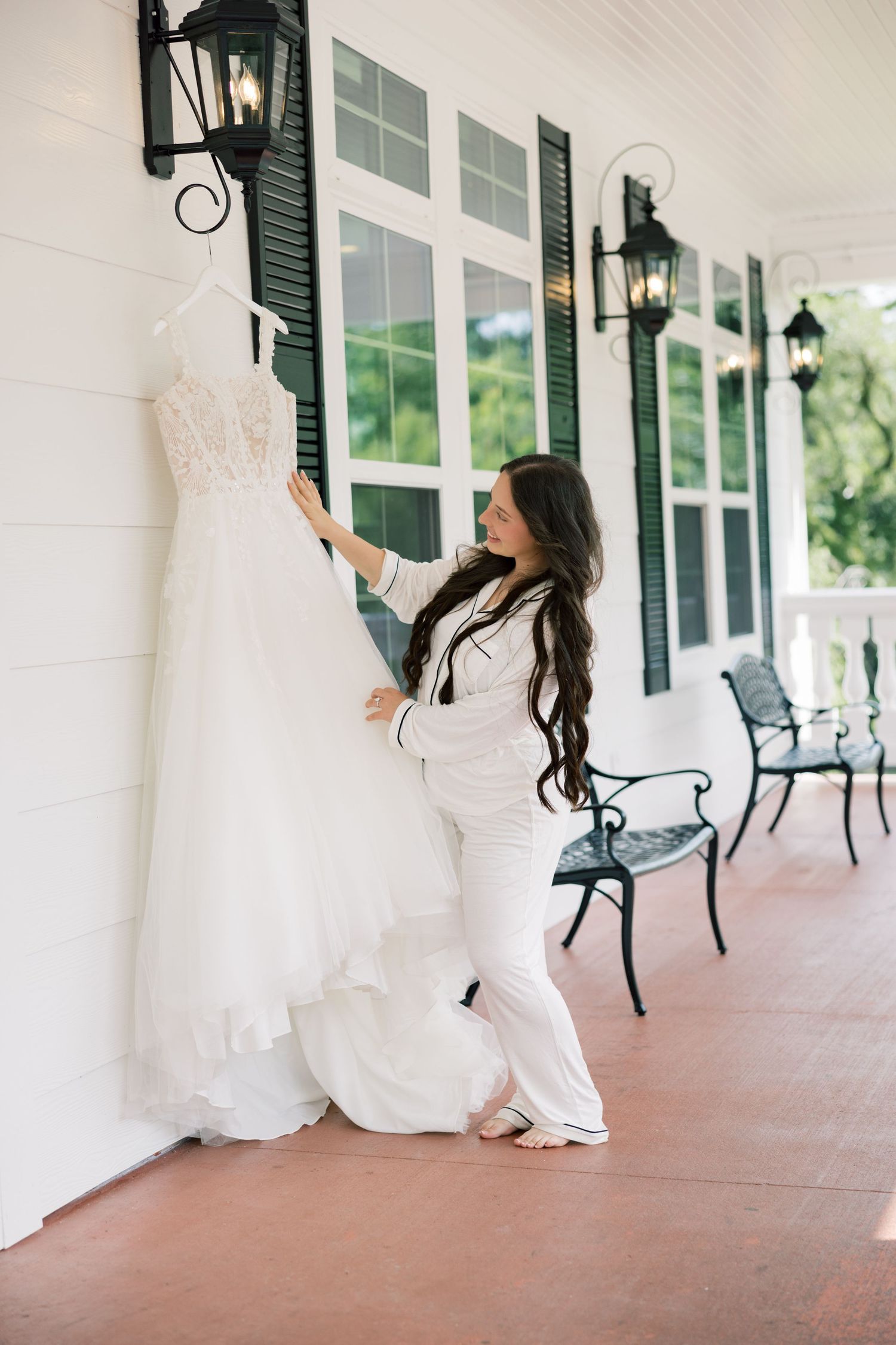 White wedding dress hanging on display along a covered porch with rocking chairs.