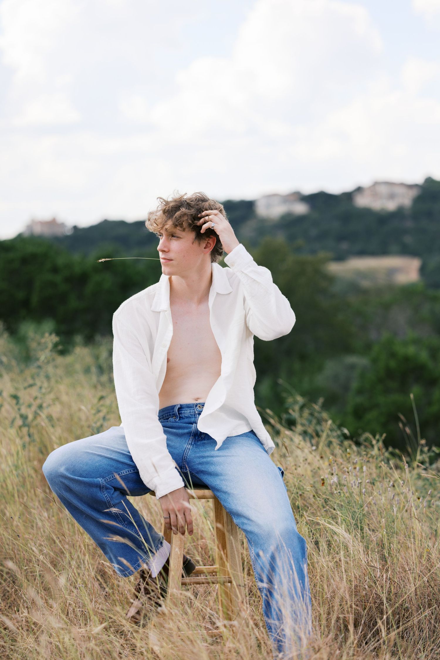 Fashion scene in a grassy field with white shirt and jeans against a natural backdrop.
