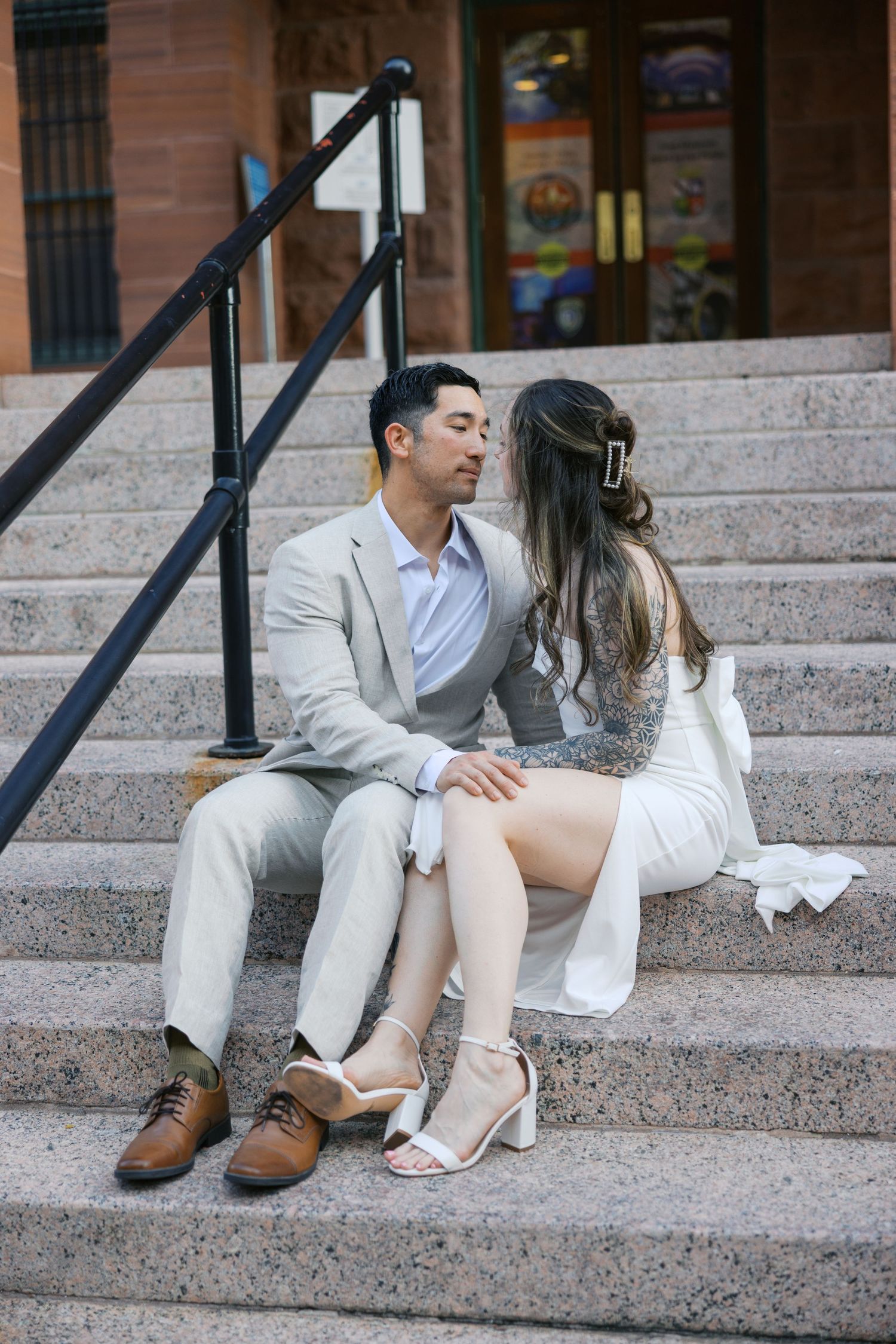 Couple in light colored outfits posing playfully on stone steps.