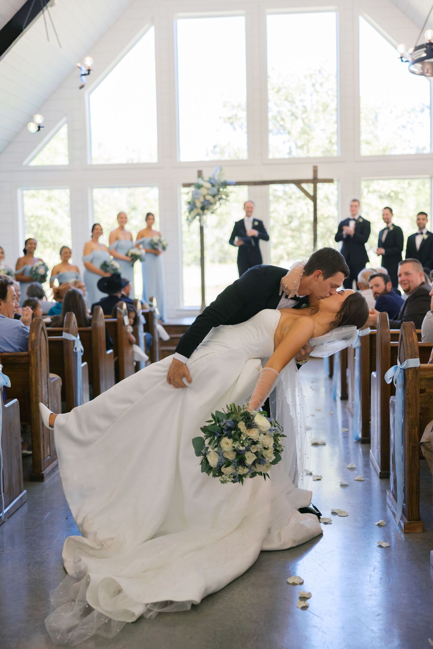 Wedding couple performs dramatic dip poses in a chapel with wooden pews and natural lighting.