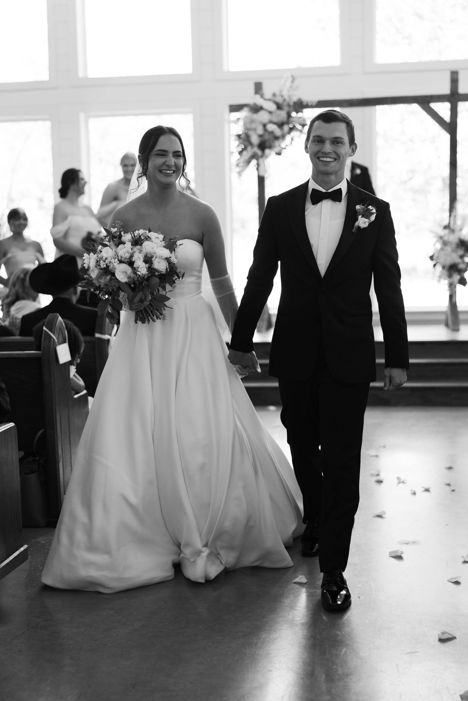 Black and white photo of newlyweds walking down aisle after wedding ceremony.