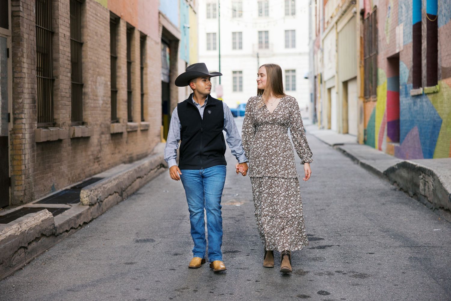 A couple walks hand in hand down an urban alley with colorful walls.
