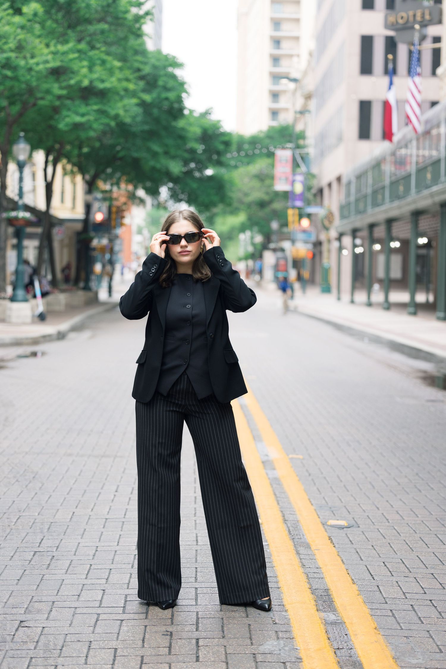 Fashion portrait on brick pavement with sunglasses and black business attire.