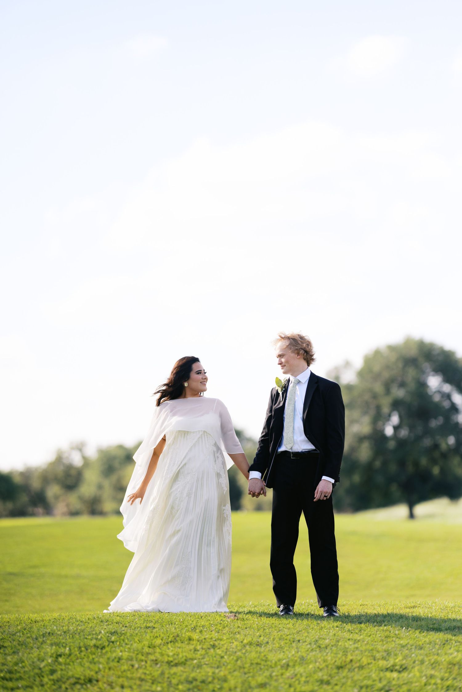 Bride and groom holding hands walking on green grass outdoors on their wedding day.