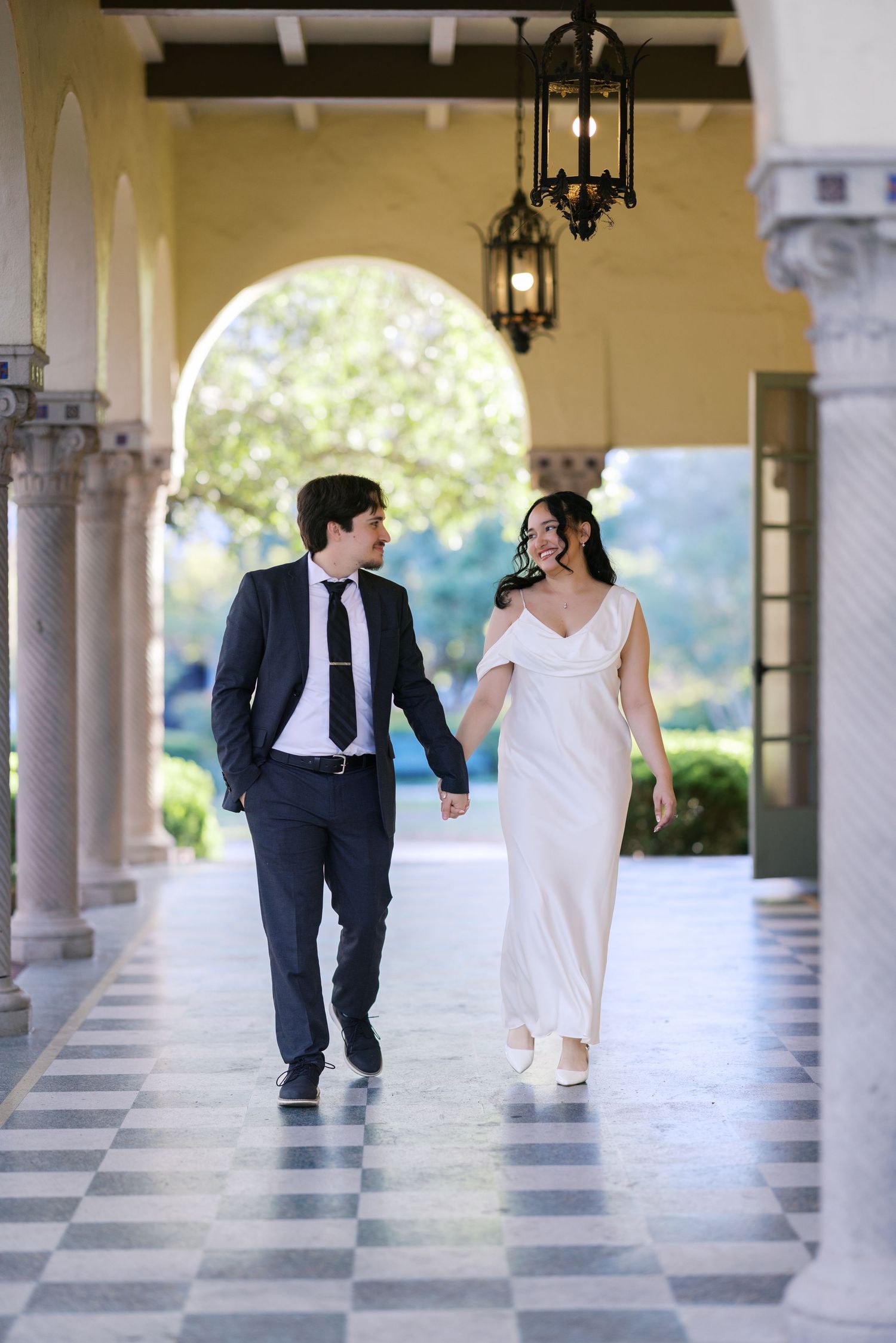 A playful wedding photo sequence along a classical colonnade with checkerboard flooring.