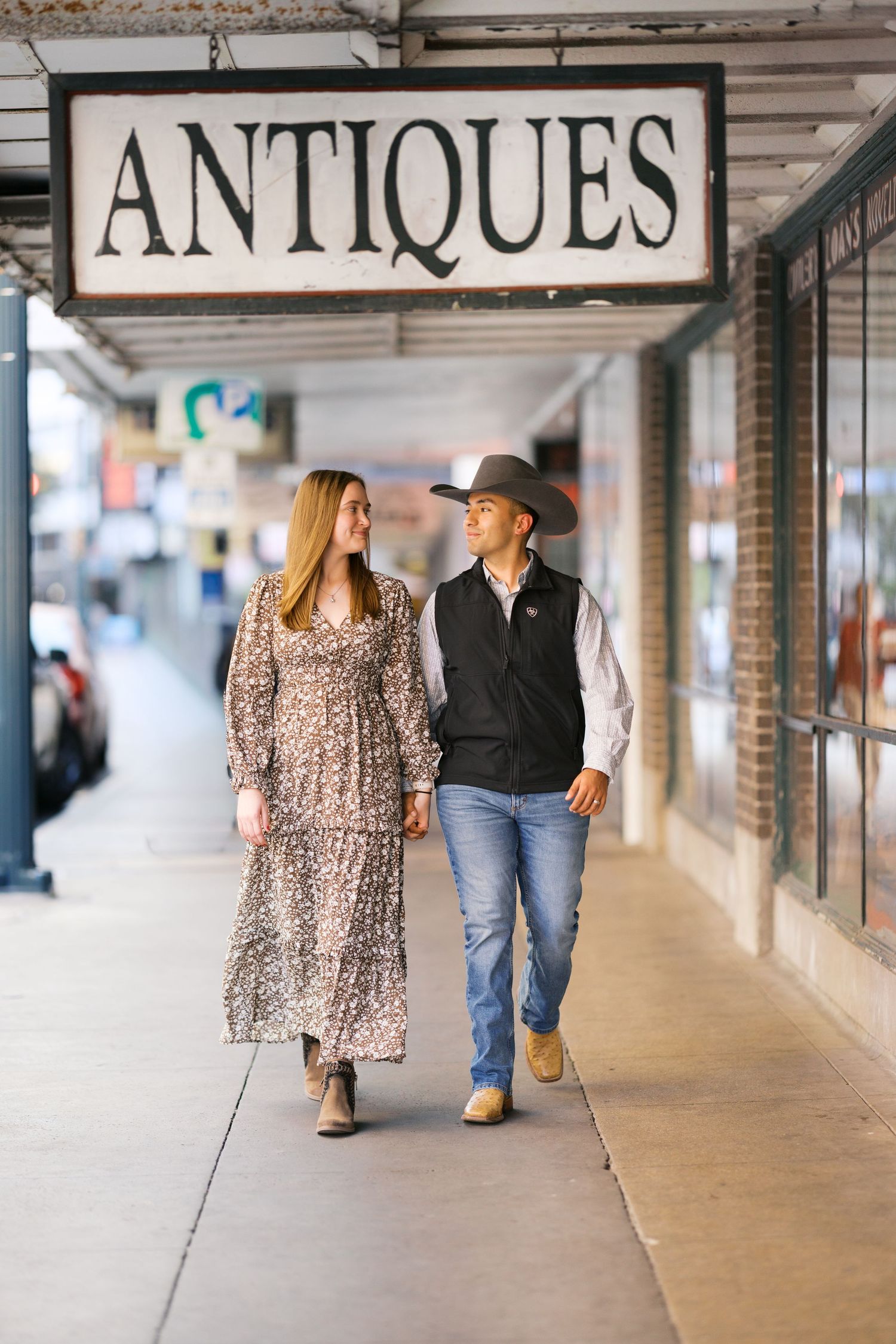 A couple strolling past antique shops under a covered walkway.