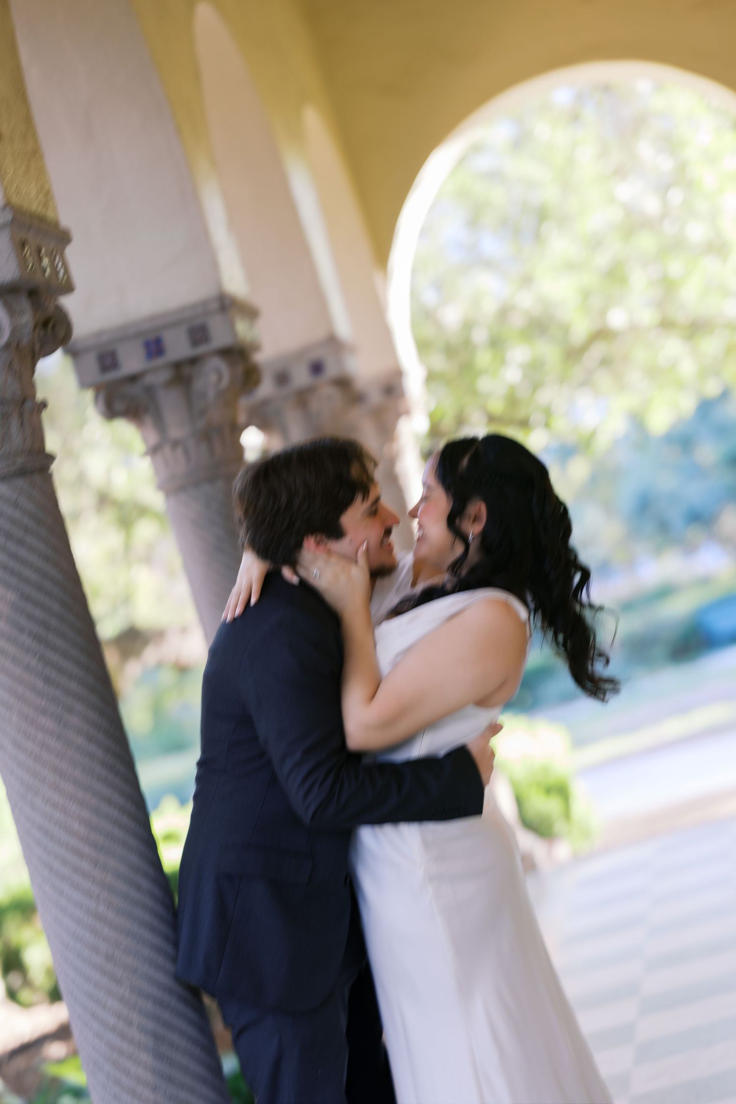 Newlyweds share intimate moments under a covered walkway with ornate columns.
