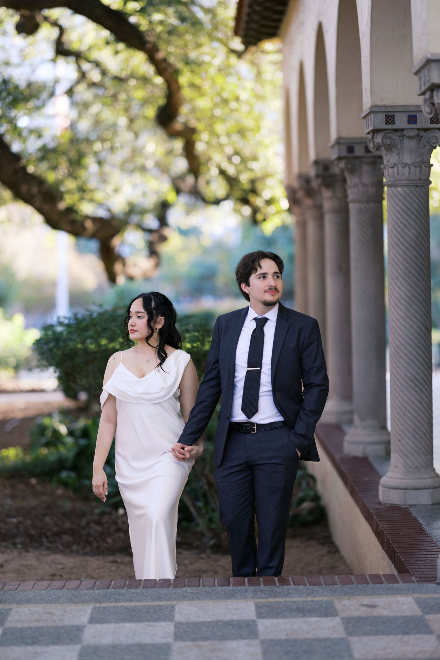 Elegant couple shares candid moments while walking along a columned archway.