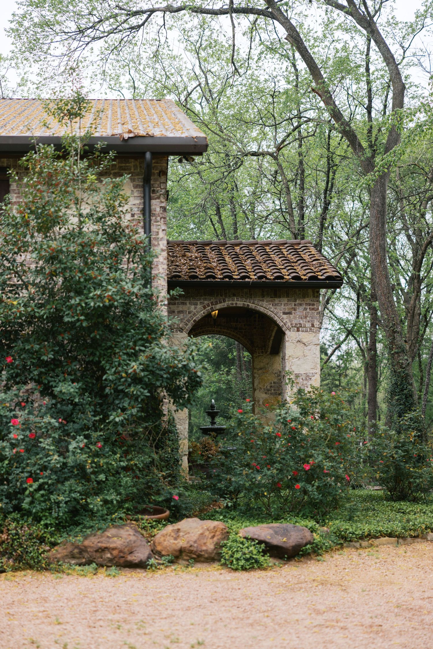 Rustic brick wedding venue with terracotta roof arch surrounded by lush greenery.
