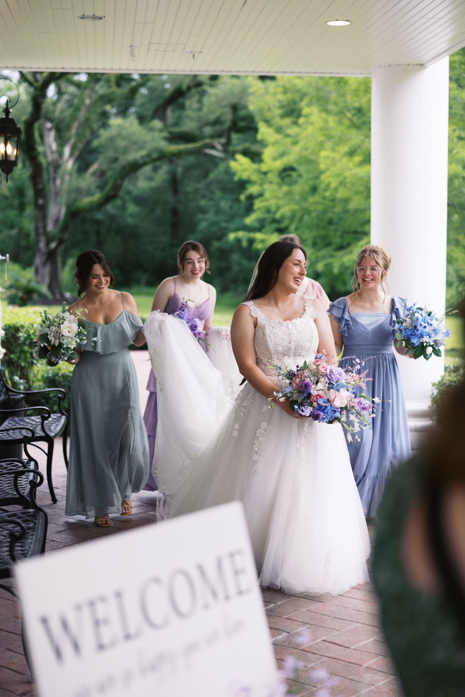 Wedding party gathered on a covered porch with welcome sign in foreground.