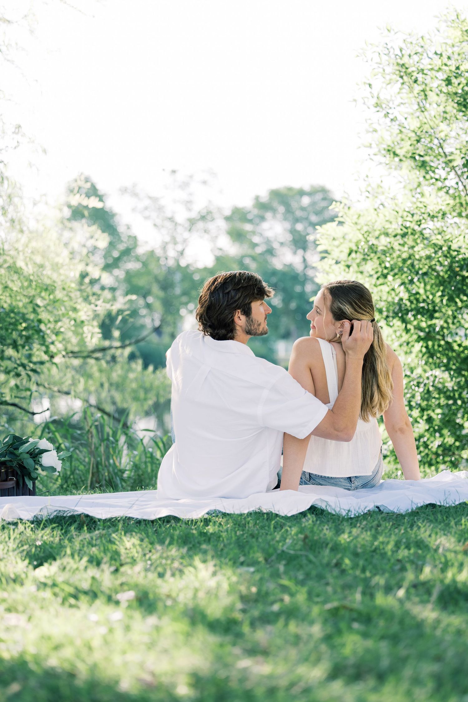 Two people relax together on a white blanket in a serene outdoor setting.