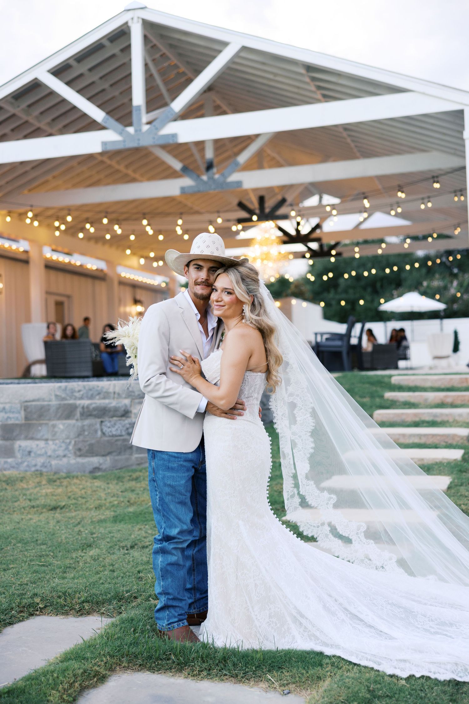 Wedding photos under covered pavilion with string lights and flowing white dress.