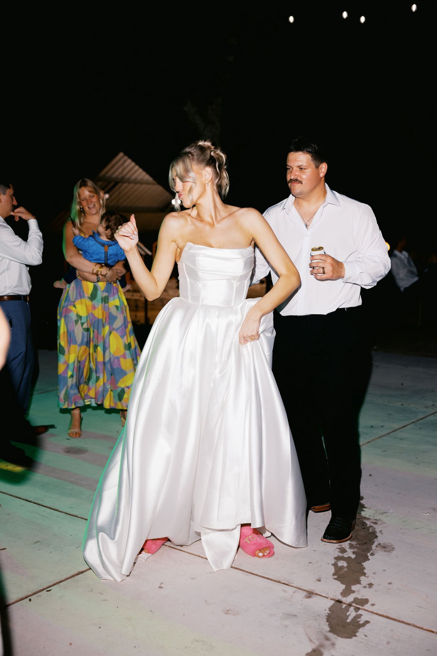 Bride in white strapless gown with pink sneakers dancing at outdoor wedding reception.