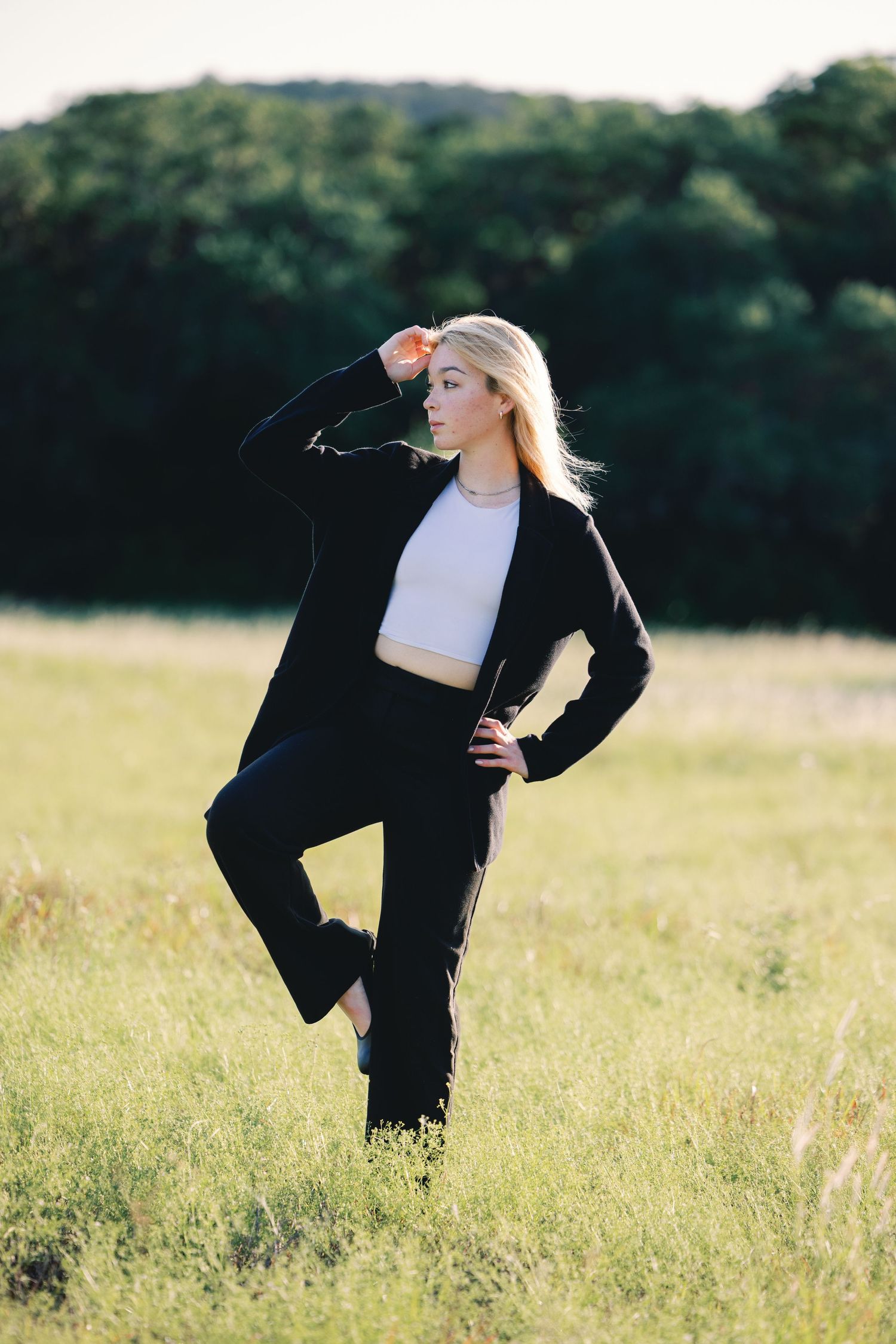 Person in black outfit dancing expressively in sunlit meadow with flowing movements.