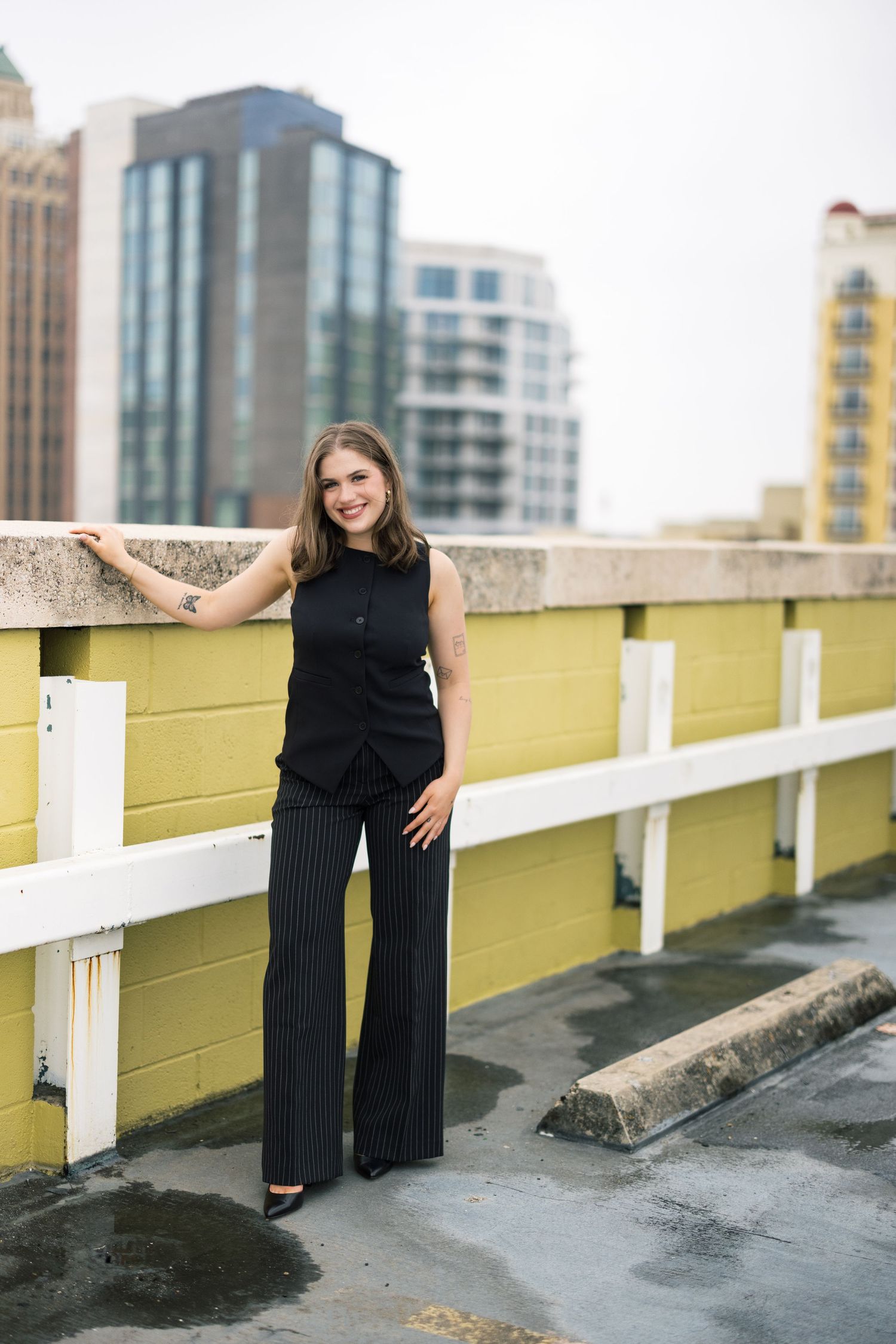Stylish black jumpsuit look photographed on a rooftop with yellow walls and white railings.