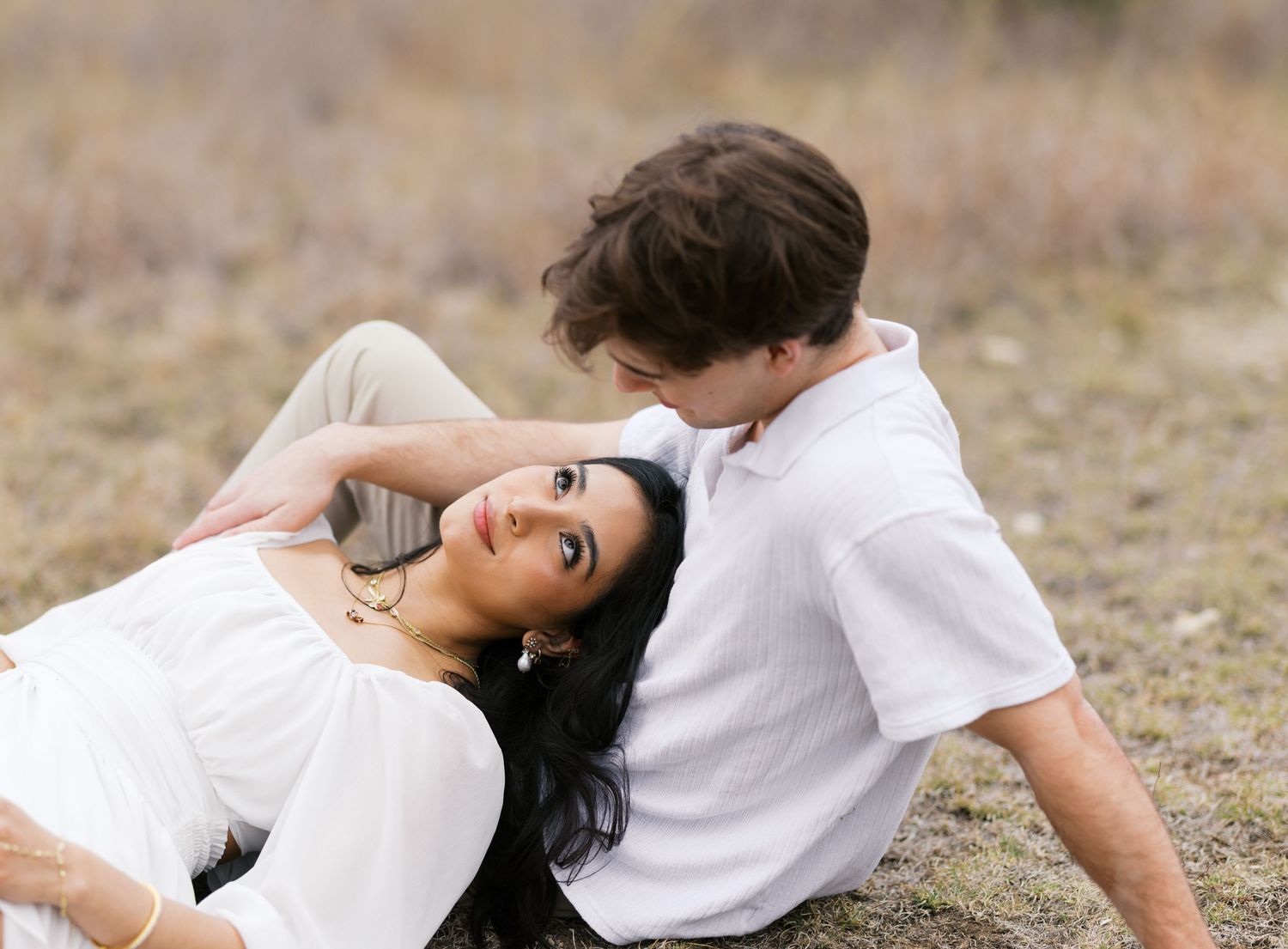 Romantic couple in casual white attire laying on ground during outdoor photoshoot.