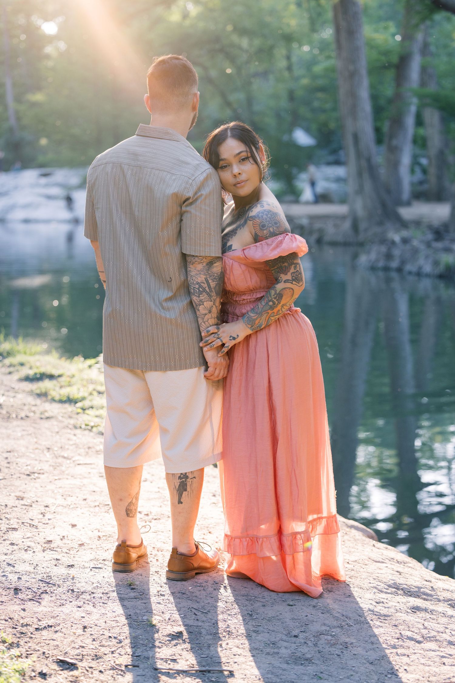 A romantic lakeside scene with a couple in coral and beige standing on rocky ground.