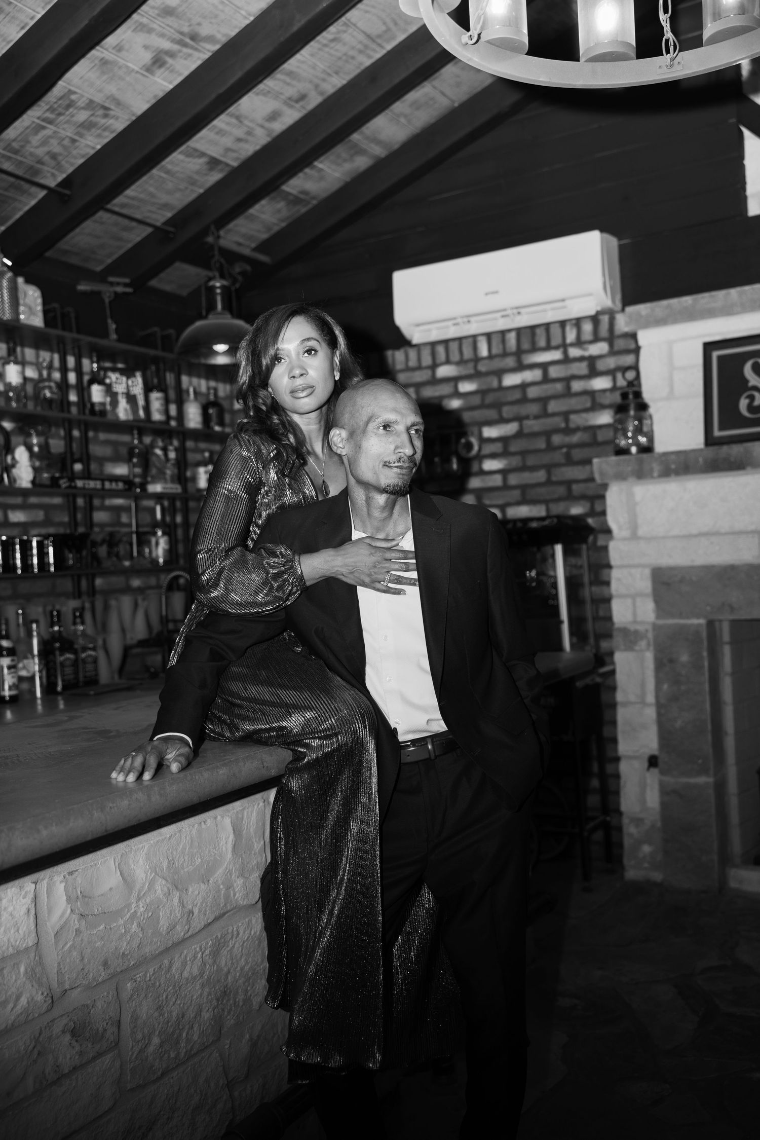 A couple shares a moment at a rustic bar with exposed beams and brick walls.