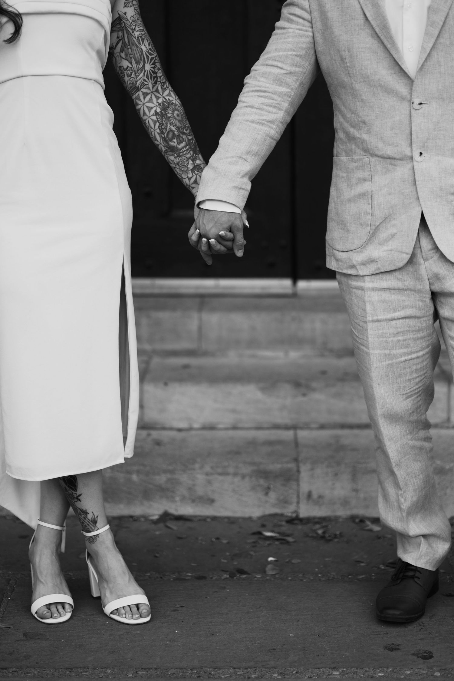 Black and white detail shot of a couple holding hands showing a tattoo sleeve and formal attire.