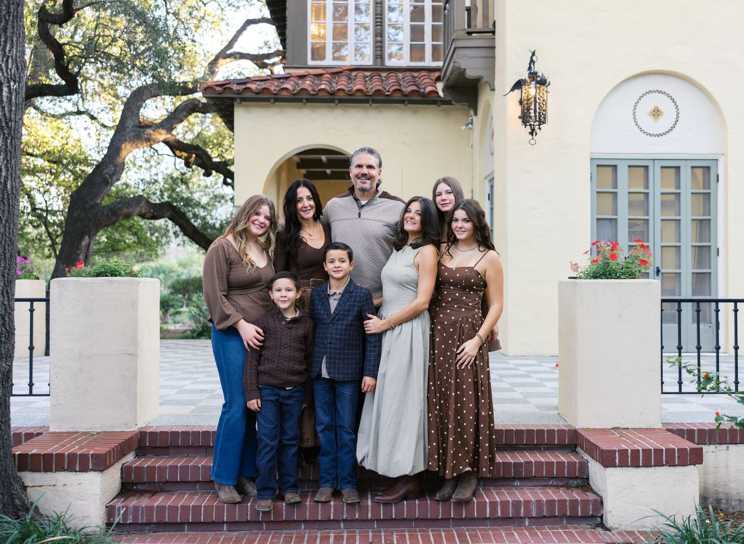 A group portrait on brick steps in front of a Spanish-style home with arched windows.
