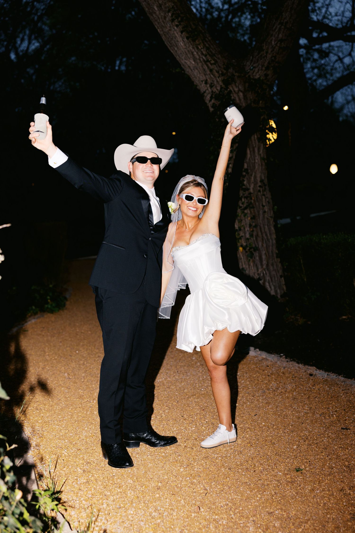 Bride and groom celebrate outdoors at night wearing sunglasses and cowboy hat.
