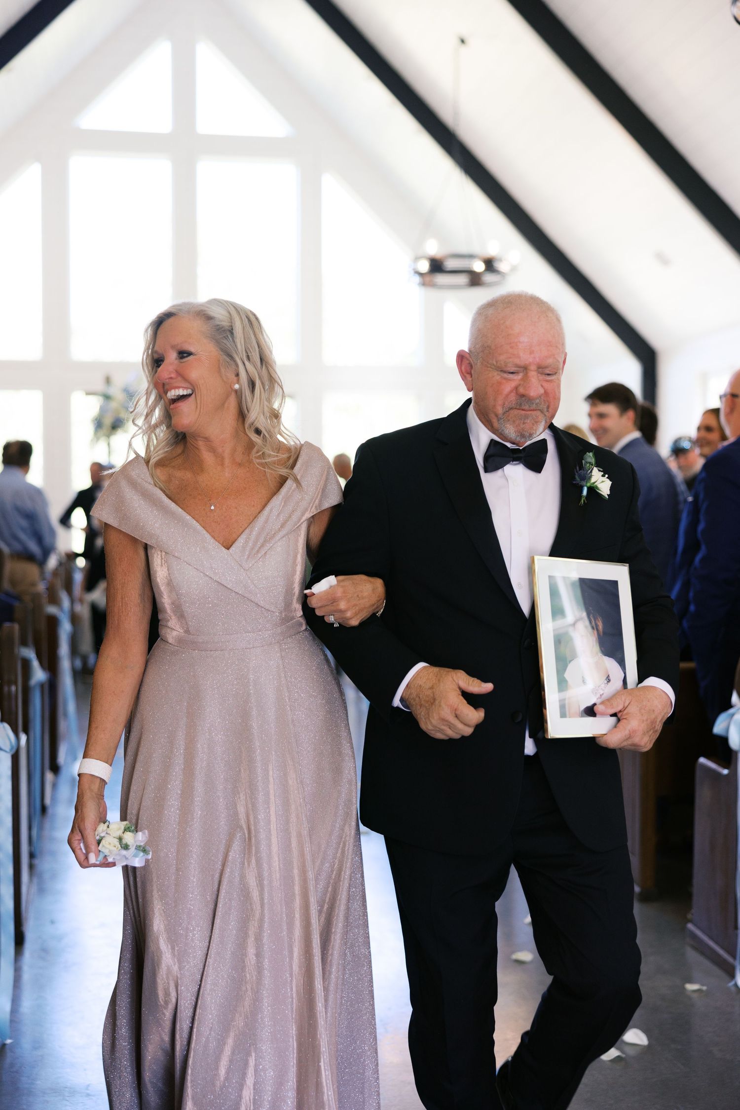 Wedding ceremony moment with pair walking down church aisle, woman in blush gown and man in tuxedo.