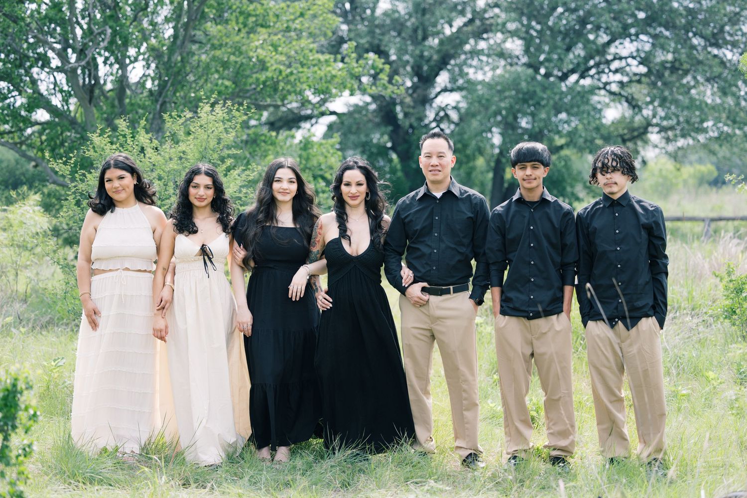Wedding party lined up outdoors wearing coordinated black and beige attire.